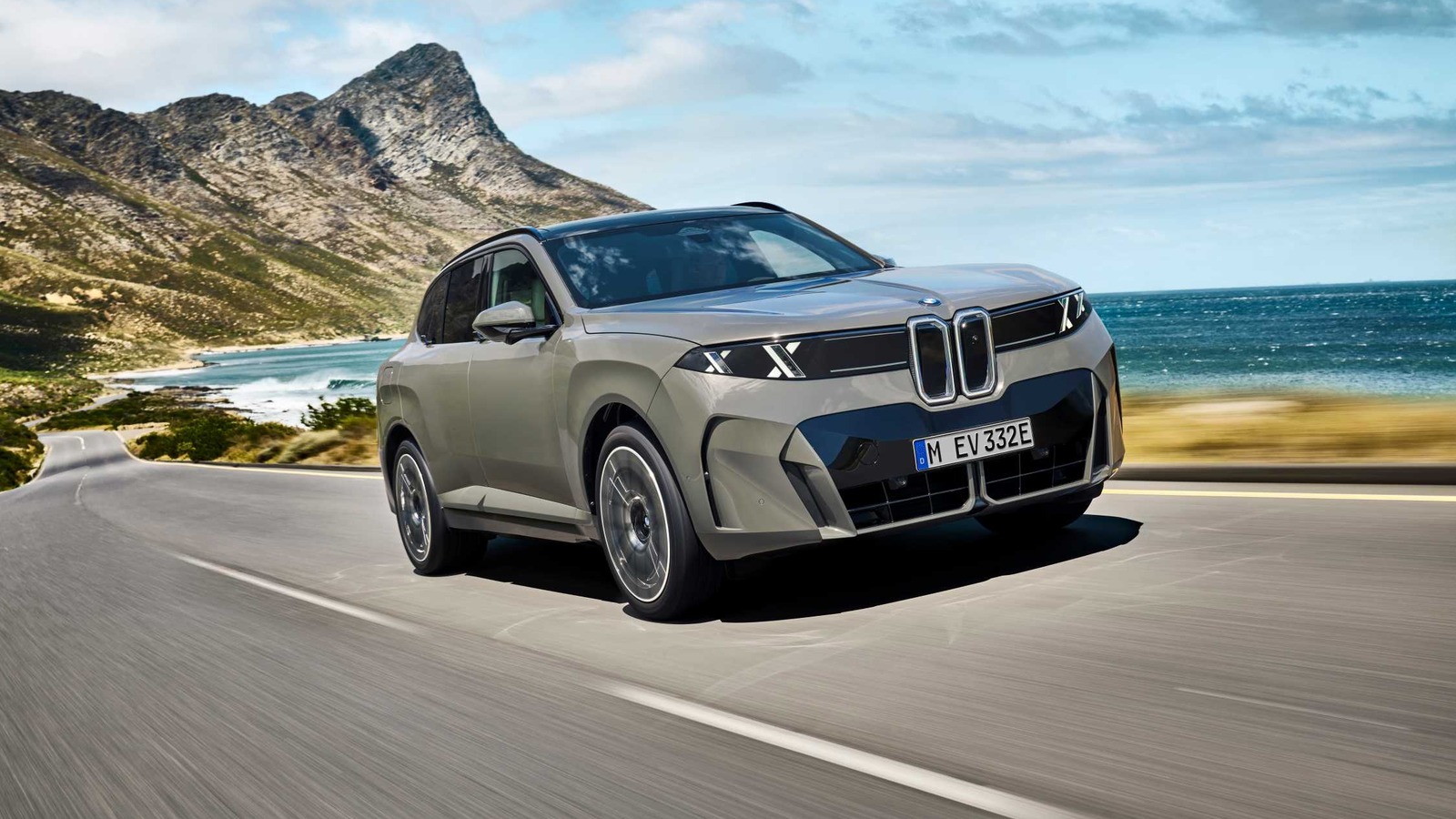 2027-bmw-ix5-60-xdrive-exterior-featured 2027 BMW iX5 60 xDrive driving along a coastal mountain road showing its illuminated vertical kidney grille and B-pillar Winglet door handles