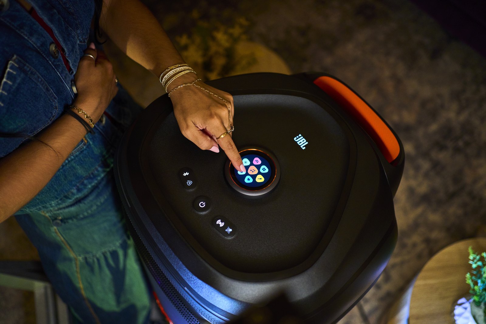 A hand using the JBL PartyBox Ultimate 2 touchscreen volume dial on the top panel