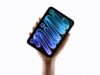 A hand holding the new midnight iPad mini, its OLED display showing blue and purple mini lettering against a black background