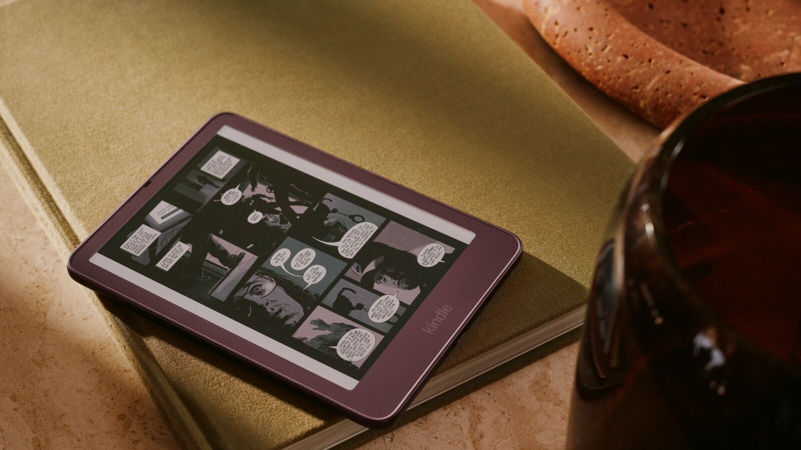 New Kindle Colorsoft in Fig red showing a comic book page while resting on a hardcover book