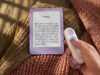New 6-inch Kindle in Ube purple on a knit blanket next to a hand holding the Kindle Click page-turn remote