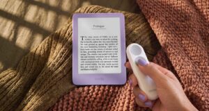 New 6-inch Kindle in Ube purple on a knit blanket next to a hand holding the Kindle Click page-turn remote