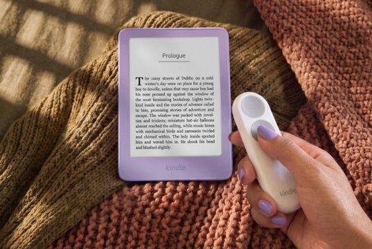 New 6-inch Kindle in Ube purple on a knit blanket next to a hand holding the Kindle Click page-turn remote