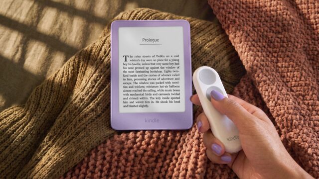 New 6-inch Kindle in Ube purple on a knit blanket next to a hand holding the Kindle Click page-turn remote
