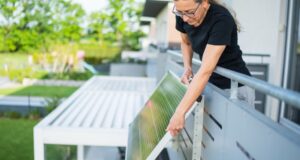 Woman attaching a plug-in solar panel to the outside of a balcony railing