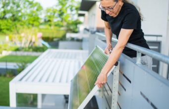 California Plug-In Solar Law Skips Utility Approval, but Caps Systems at 1,200 Watts Woman attaching a plug-in solar panel to the outside of a balcony railing