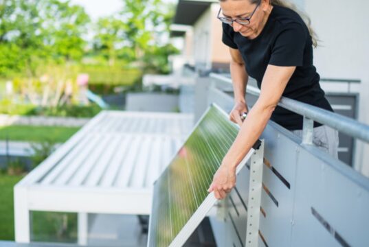 Woman attaching a plug-in solar panel to the outside of a balcony railing