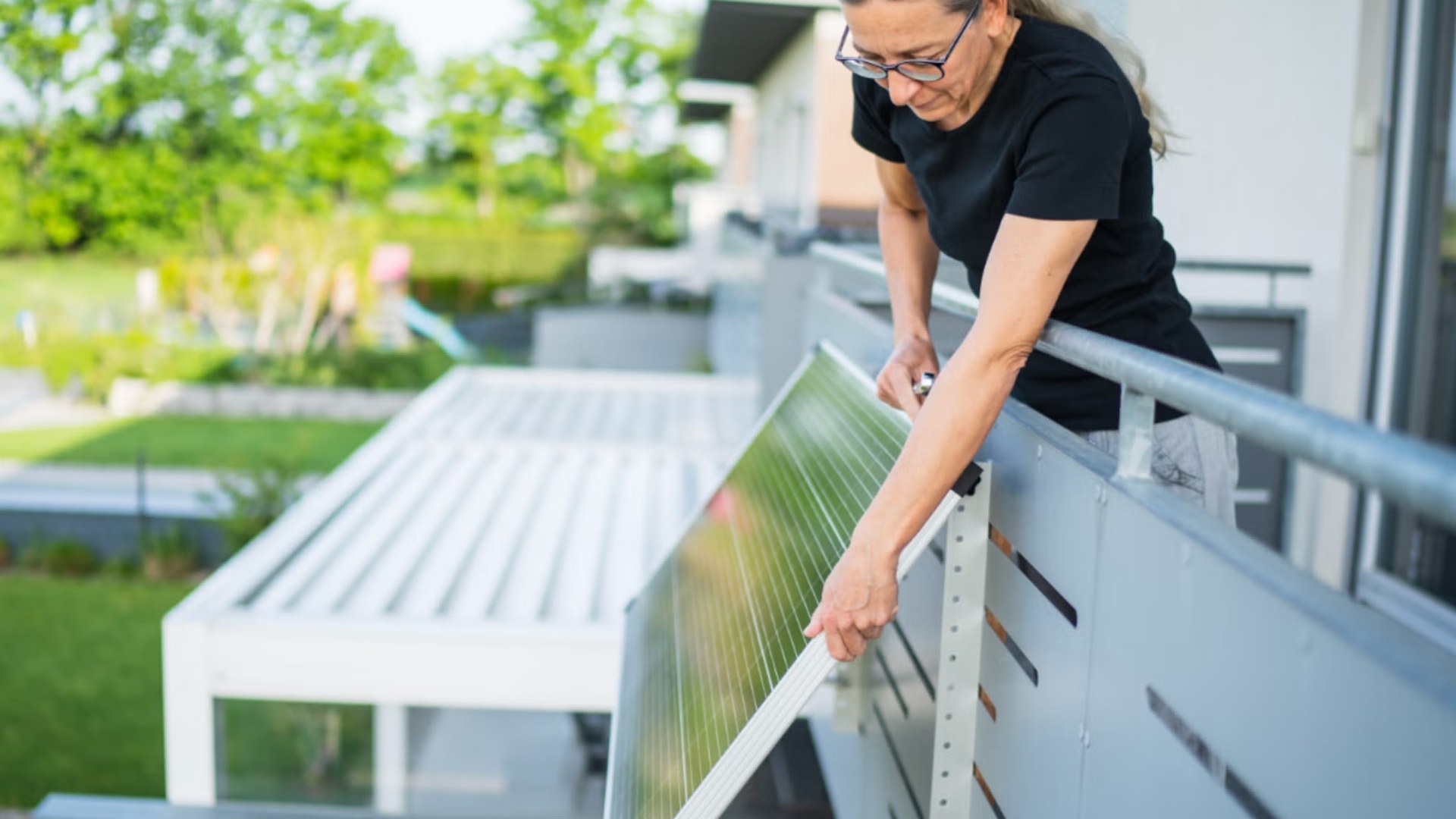 plug-in-solar-panel-balcony-ul-solutions Woman attaching a plug-in solar panel to the outside of a balcony railing