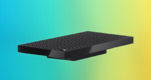 Surface RTX Spark Dev Box angled on a blue, purple and yellow gradient backdrop, showing the perforated top and the Microsoft logo
