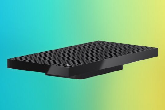 Surface RTX Spark Dev Box angled on a blue, purple and yellow gradient backdrop, showing the perforated top and the Microsoft logo
