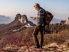 Hiker with a backpack using a smartphone on a remote mountain ridge at sunset
