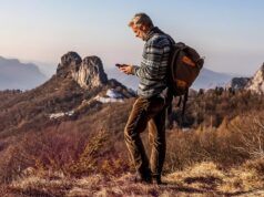Satellite Joint Venture From AT&T, T-Mobile and Verizon Has a CEO but No Launch Date Hiker with a backpack using a smartphone on a remote mountain ridge at sunset