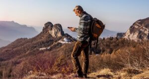 Hiker with a backpack using a smartphone on a remote mountain ridge at sunset