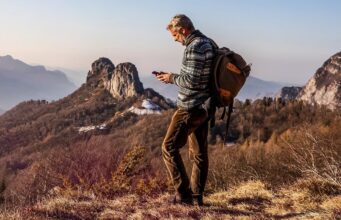 Satellite Joint Venture From AT&T, T-Mobile and Verizon Has a CEO but No Launch Date Hiker with a backpack using a smartphone on a remote mountain ridge at sunset