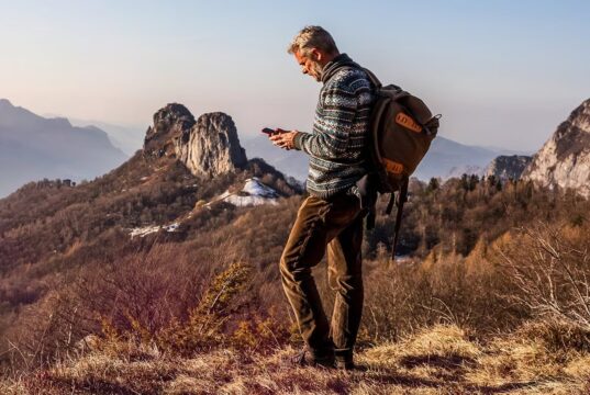 Hiker with a backpack using a smartphone on a remote mountain ridge at sunset