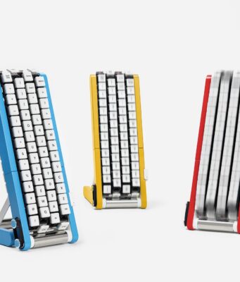 Google Japan’s Gboard Conveyor Belt Keyboard Brings the Keys to You Three conveyor-belt keyboards on stands in blue, yellow and red, each with white keycaps mounted on four vertical belts; the red unit's belts are blurred with the keys in motion