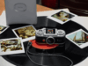 Instax Pal 2 camera on a vinyl record beside instant prints and a separate printer
