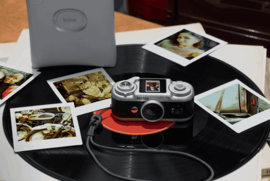 Instax Pal 2 camera on a vinyl record beside instant prints and a separate printer