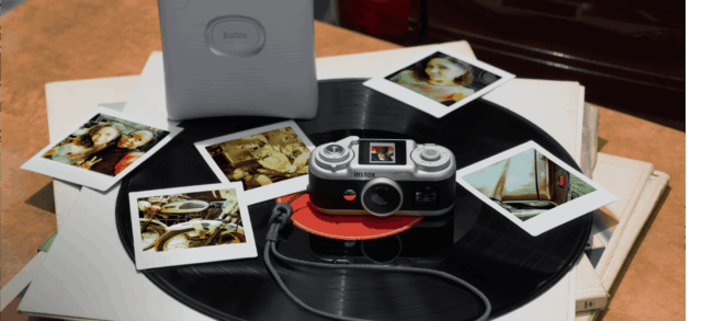 tmm-instax-pal-2-official-hero Instax Pal 2 camera on a vinyl record beside instant prints and a separate printer
