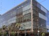 OpenAI Engineer Charged Over Hidden Recording Device in Executive Room Glass-fronted office building at 1515 Third Street in San Francisco's Mission Bay, with palm trees and a traffic signal at the corner