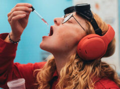 Skullcandy Stays Separate After Bose Buys the Brand A person in a red shirt and orange headphones holds a dropper of pink liquid near an open mouth, with black goggles on their forehead