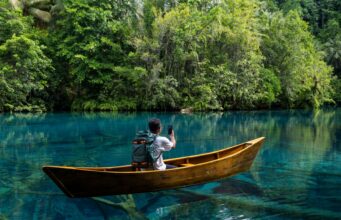 SpaceX Agrees to Buy 800 MHz Spectrum That Could Make Starlink Mobile a Major Carrier A person seated in a wooden canoe on a clear river, filming a dense jungle shoreline with a smartphone