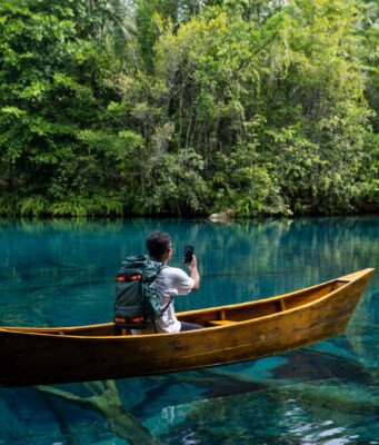 SpaceX Agrees to Buy 800 MHz Spectrum That Could Make Starlink Mobile a Major Carrier A person seated in a wooden canoe on a clear river, filming a dense jungle shoreline with a smartphone