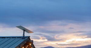 Starlink Residential vs Roam $55 monthly US plans use the same price for different service Starlink dish mounted on a green metal roof with string lights at dusk, fields and mountains behind it