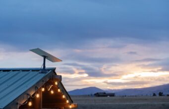 Starlink Residential vs Roam $55 monthly US plans use the same price for different service Starlink dish mounted on a green metal roof with string lights at dusk, fields and mountains behind it