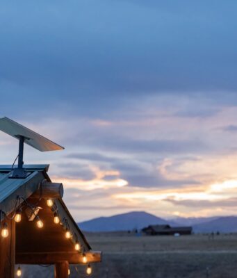 Starlink Residential vs Roam $55 monthly US plans use the same price for different service Starlink dish mounted on a green metal roof with string lights at dusk, fields and mountains behind it