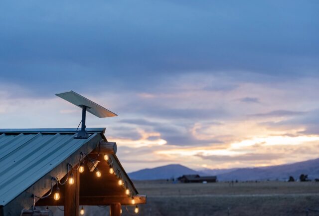 tmm-starlink-residential-vs-roam-featured Starlink dish mounted on a green metal roof with string lights at dusk, fields and mountains behind it