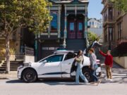 White Waymo Jaguar I-PACE robotaxi parked on a San Francisco street with riders loading the trunk