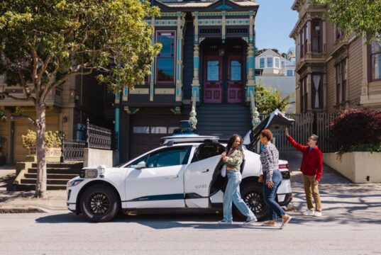 White Waymo Jaguar I-PACE robotaxi parked on a San Francisco street with riders loading the trunk