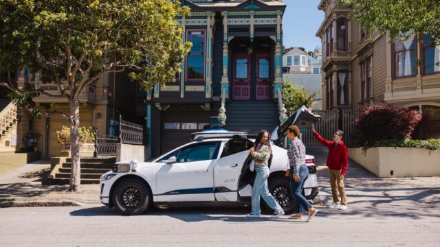 White Waymo Jaguar I-PACE robotaxi parked on a San Francisco street with riders loading the trunk